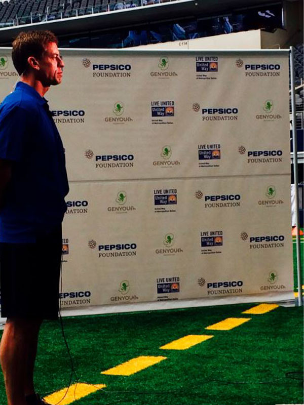 Troy Aikman standing in front of a step and repeat banner