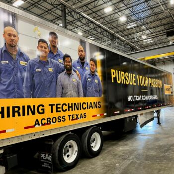 Side of semi trailer wrapped in car vinyl with company team and promotional text.