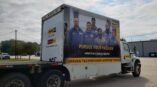 The side of a box truck wrapped in vinyl with a picture of a team and promotional text and company logo