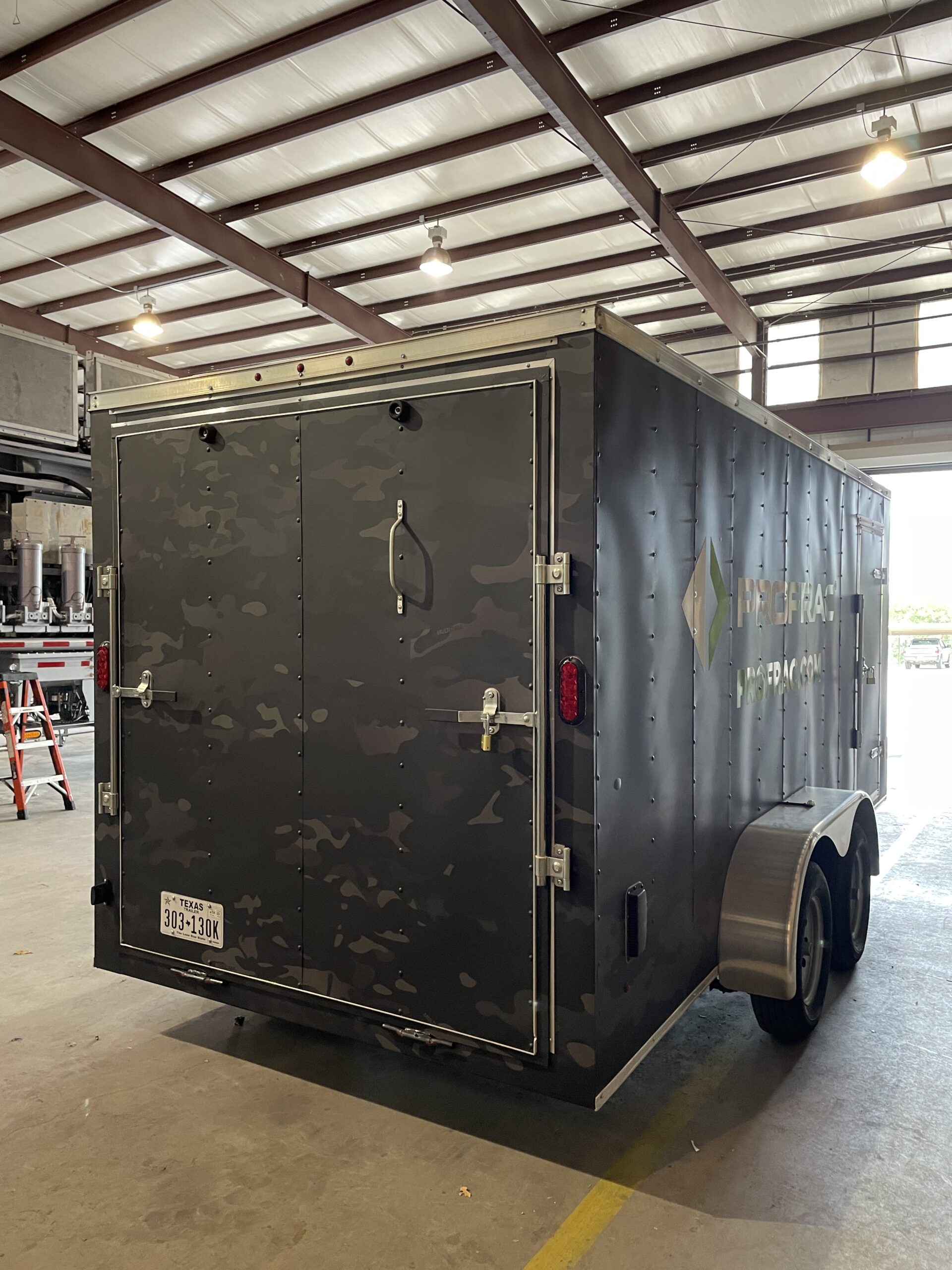 Back side of a trailer with black panel car wrap with company logo and camo graphics.