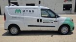 Right side of a van that is wrapped in green graphics with a logo and promotional text.
