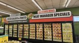 Custom-printed commercial interior signage for a grocery store, with bold graphics above refrigerated cases advertising 