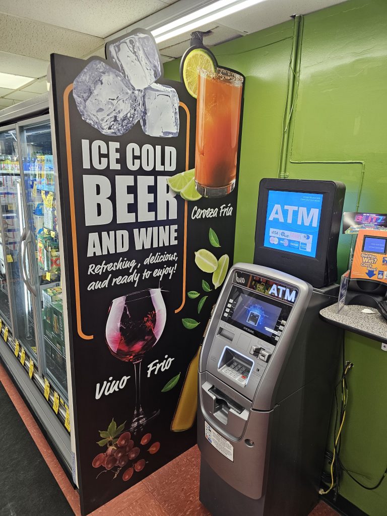 Commercial retail graphic advertising "Ice Cold Beer and Wine" with images of drinks, placed next to an ATM and refrigeration units, a custom print job by SpeedPro Irving.