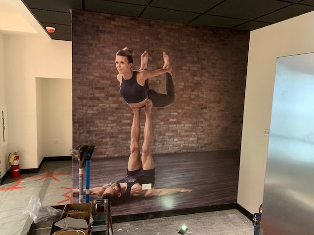 Large wall mural of two people performing acro yoga on a brick background in Chicago, IL.