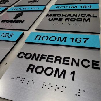 Braille ADA room identification signs with raised text and symbols on metal panels in Chicago, IL.