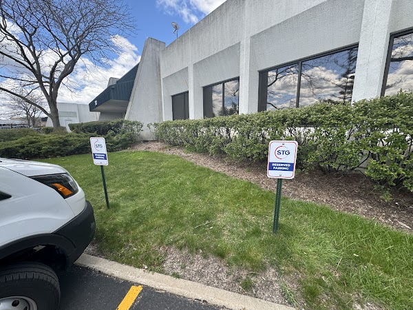 Two metal reserved parking signs with posts in a grassy area outside a building in Chicago, IL.