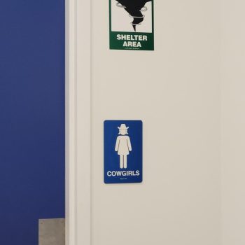 Blue ADA bathroom sign with female figure and hat and green severe weather shelter area sign on