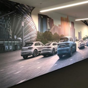A wall mural with 5 cars driving down a city street with high rise next to the street
