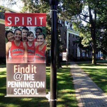 Sign on courtyard pole with 5 female cross country runners for Pennington High School showing spirit