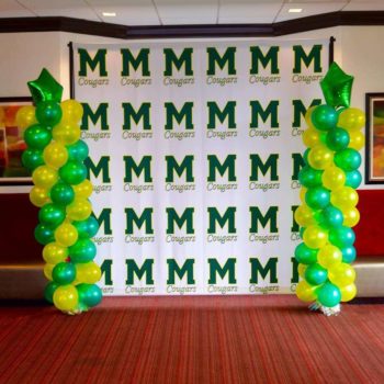 Banner with green logos for the M. Cougars and balloons on either side.