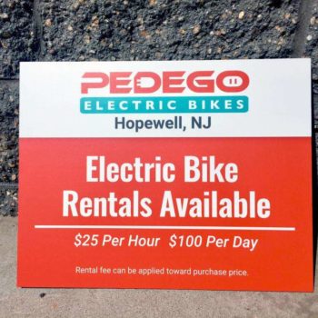 Outdoor advertisement sign for Pedego Electric Bikes. They offer rates of $25 per hour and $100 per day.