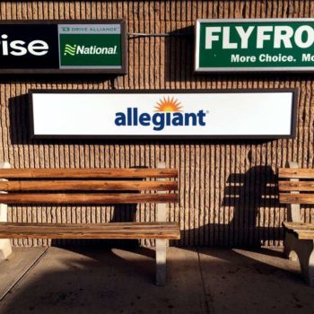 Outdoor signs for Enterprise, National, Allegiant, and Fly Frontier on a brick wall
