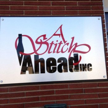 Sign on brick wall for A Stitch Above, Inc.