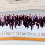 Wall portrait with men and women in business dress. Underneath them, it states "heart of the community."