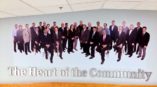 Wall portrait with men and women in business dress. Underneath them, it states 
