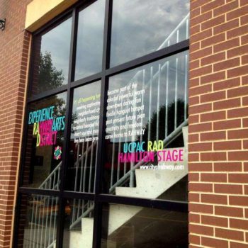 Window graphic advertising an arts district in pink, blue, yellow and white font