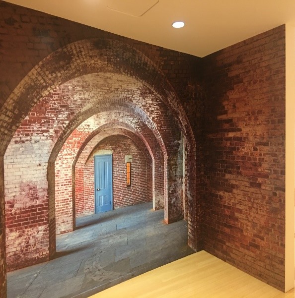 Wall mural of four brick arches leading down a pathway to a blue door