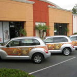 Line of three silver PT-Cruisers with decal featuring Panera bread logo and catering information 