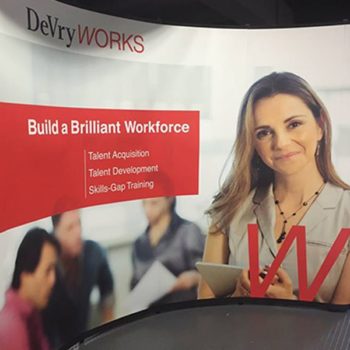 Tradeshow display featuring a banner for DeVry with image of woman with a clipboard 