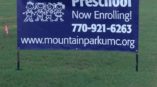 Outside banner advertising Mountain Park UMC Preschool Enrollment with cartoon images of children 