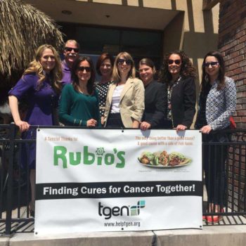 A group of people smiling behind a banner thanking a restaurant for sponsoring cancer research