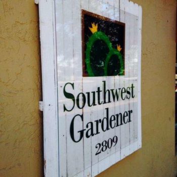 Outdoor glass sign in front of white fencing on a wall for 