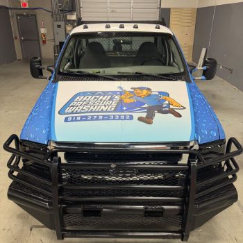 Front view of a custom truck wrap featuring bold blue graphics and illustrated branding for a pressure washing company.