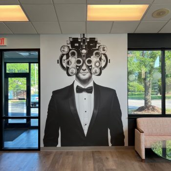 Large wall mural of a man in a tuxedo with an eye exam phoropter in an office in Raleigh, NC.