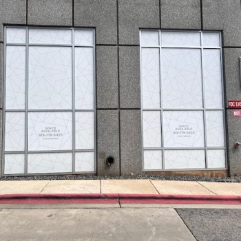 Two large commercial windows with patterned privacy window films on a gray building in Raleigh, NC.