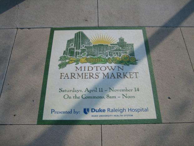 Midtown Farmers Market sidewalk sign with event dates and sponsor details.