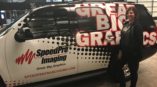 Woman standing next to black sedan covered with SpeedPro Imaging vehicle wrap