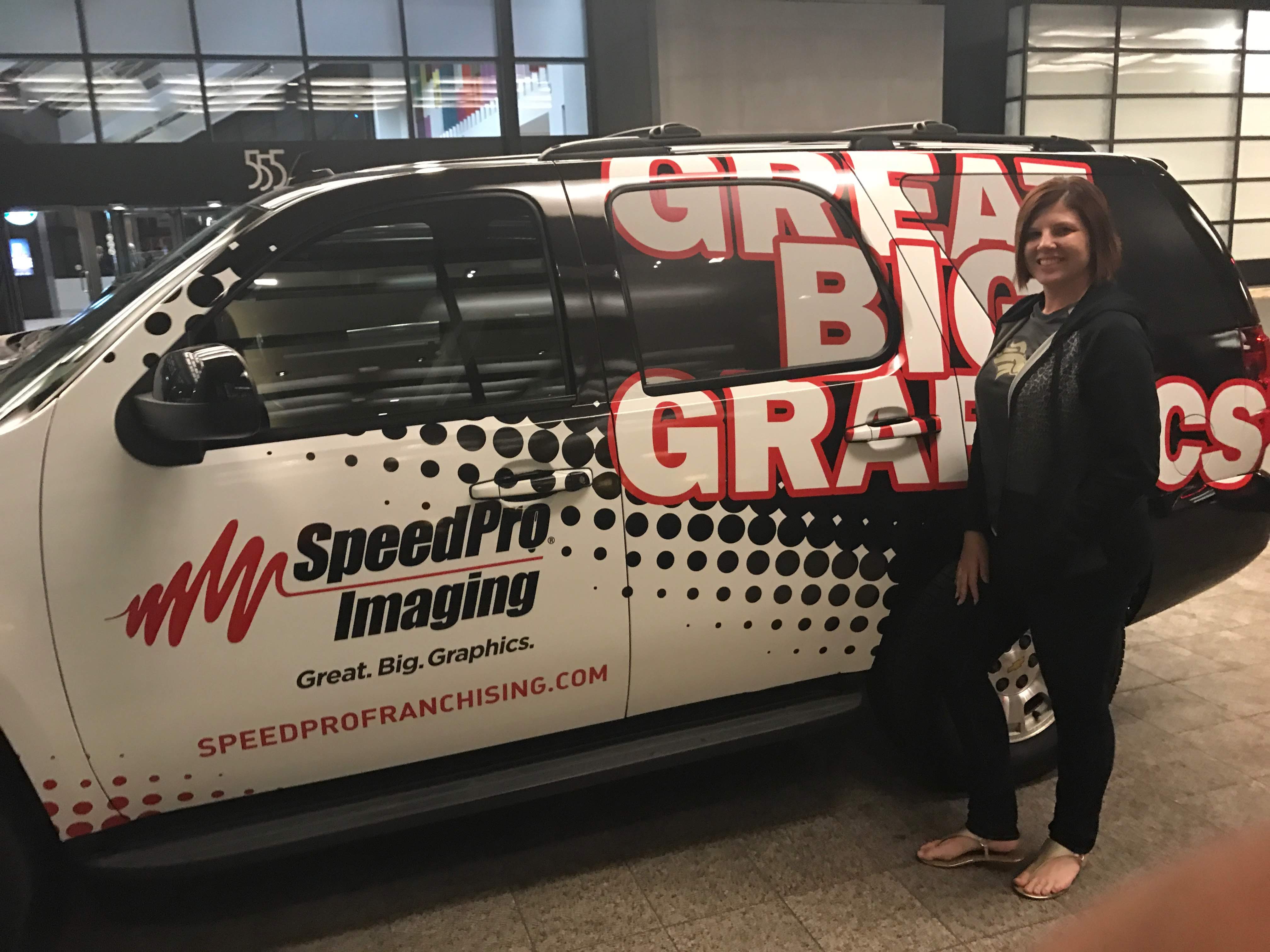 Woman standing next to black sedan covered with SpeedPro Imaging vehicle wrap
