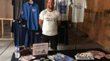 man standing behind booth  with tshirts behind him for armed forces families foundation