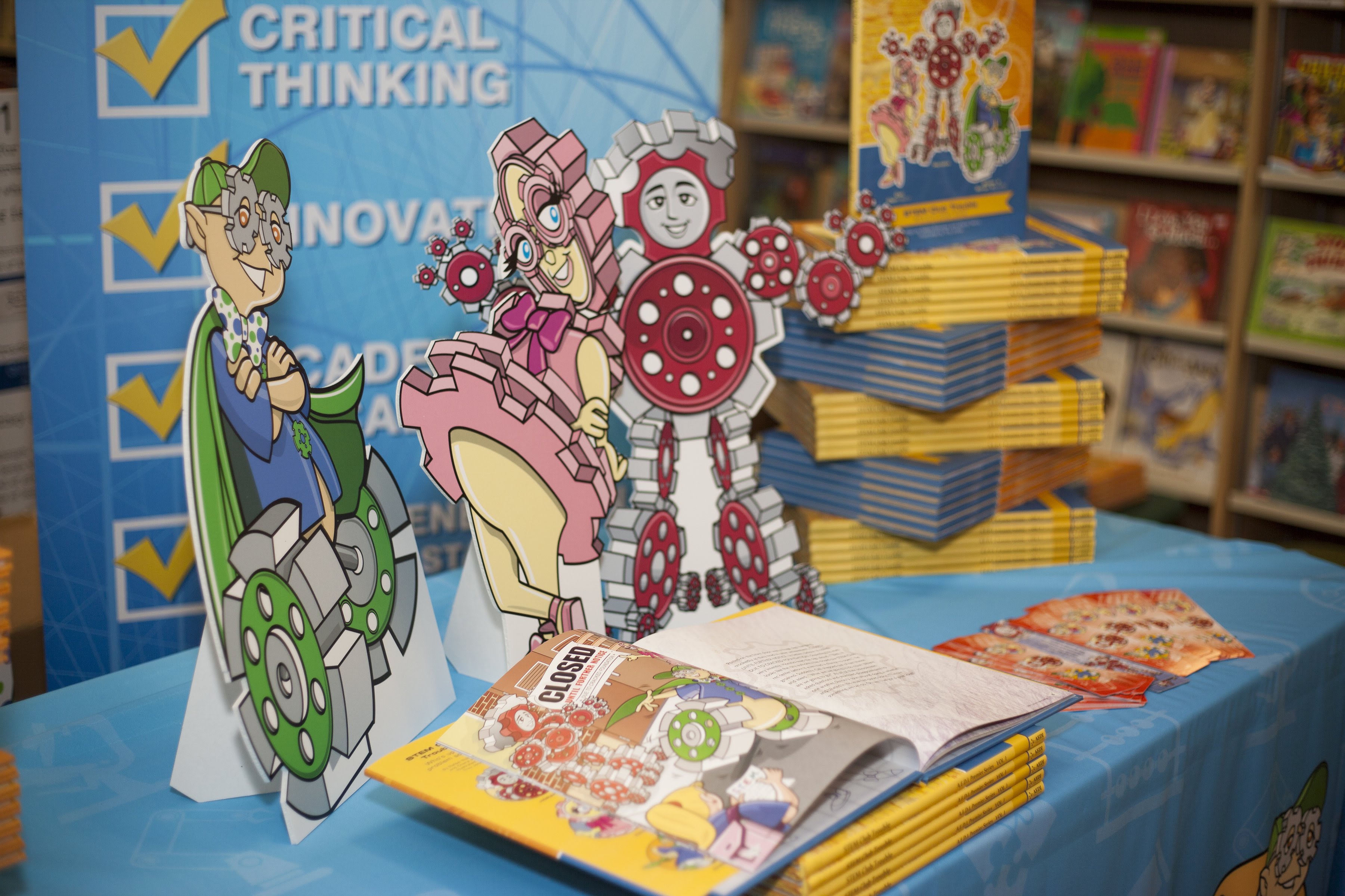 three cartoon characters that look like gears surrounded by books
