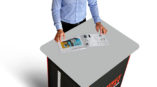man in blue dress shirt standing behind expolinc double case counter with silver top