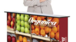 woman standing in front of table covered with image of apples and oranges for organica whole foods