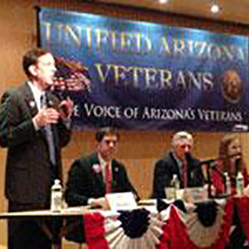 A speaker behind a podium with a Veterans banner behind him