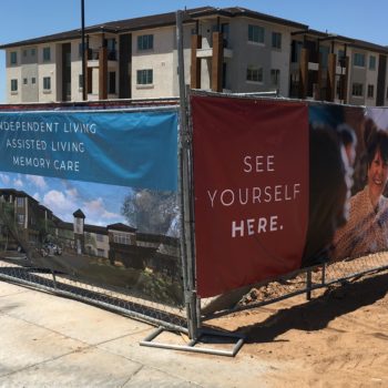 Colorful imagery and text on fence banners in front of an assisted living construction site