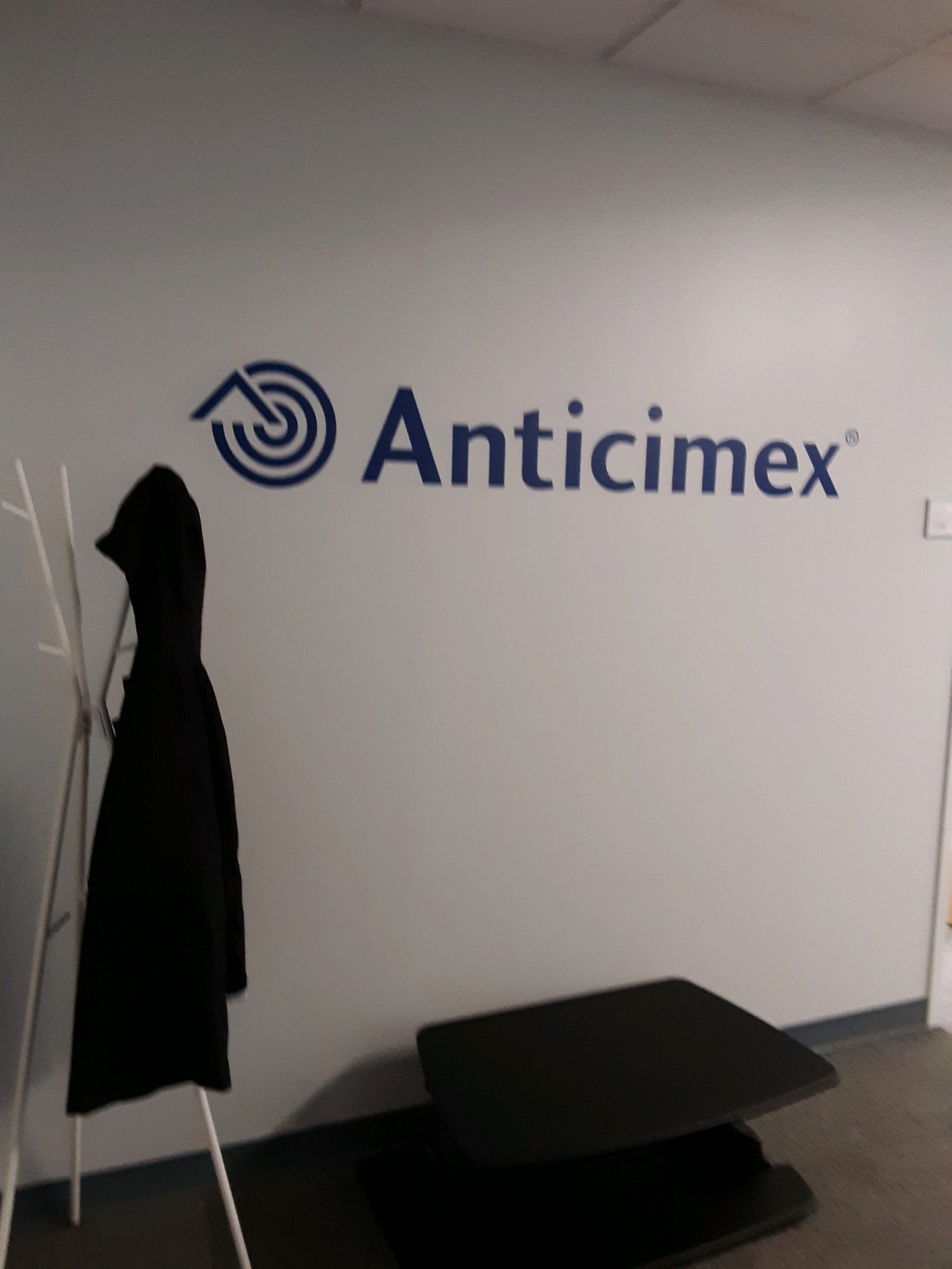 Anticimex written in blue on white wall with coat hanger in front of it with a black coat