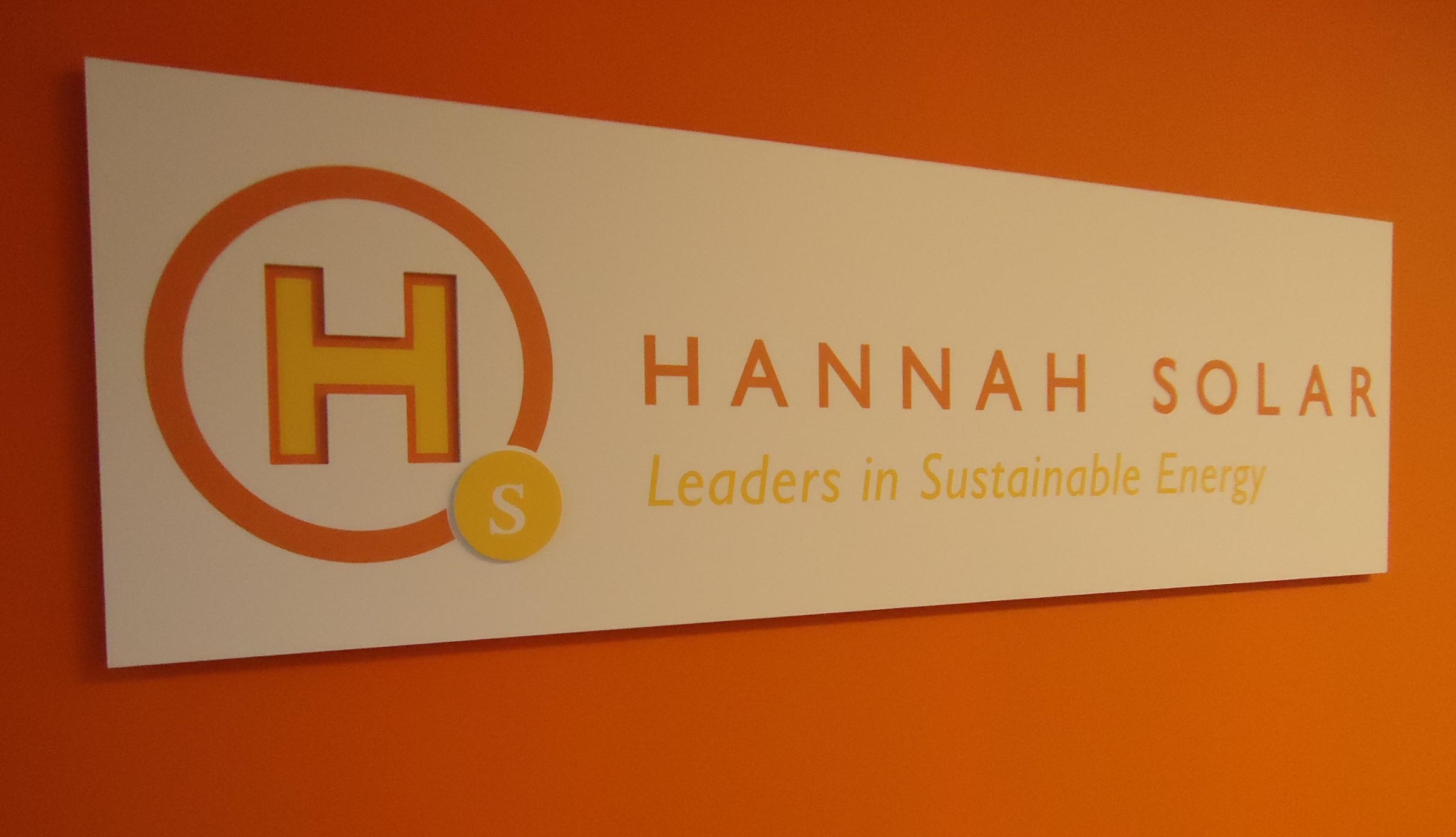 Orange wall with white sign that says Hannah Solar in orange and Leaders in Sustainable Energy in yellow.