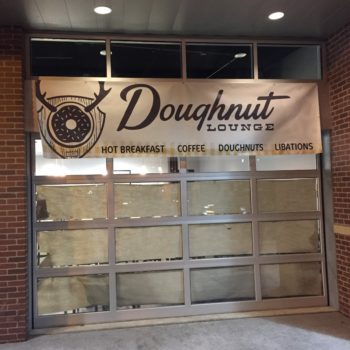 Outdoor banner sign advertising Doughnut Lounge hung on a window outside of the building 
