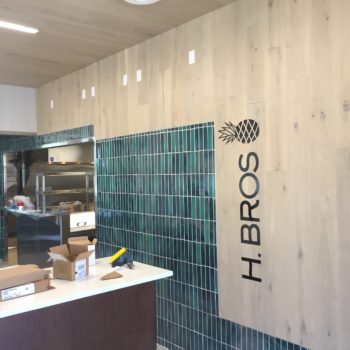 Tile wall with wood paneling features the Hawaiian Bros. logo with an illustrated black pineapple