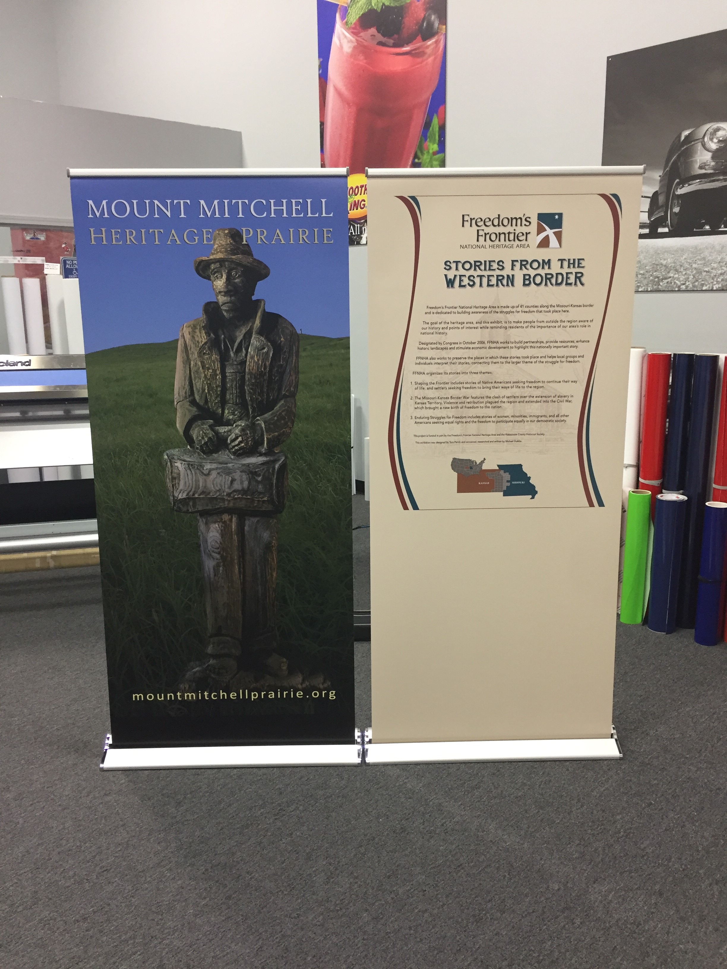 Two banners side by side one advertising Mount Mitchell Heritage Prairie with statue and the other for Freedom's Frontier  