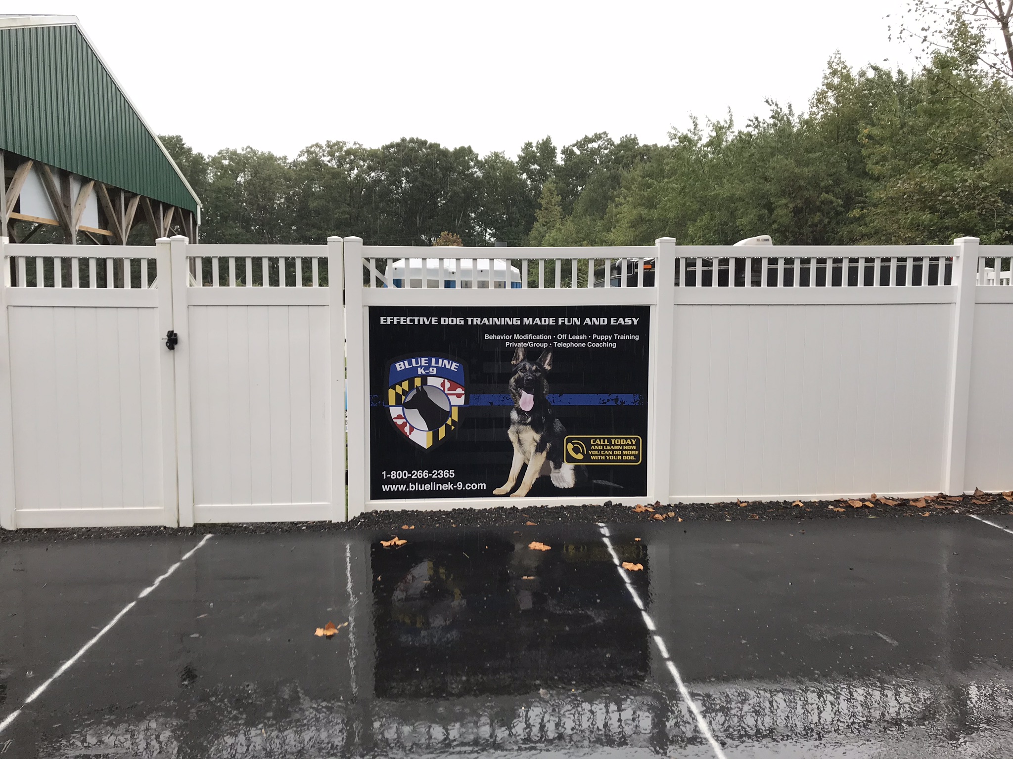 Outdoor sign on a white fence for Blue Line K-9 with image of German Shepherd and logo 