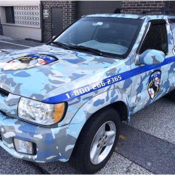 Vehicle wrap for Blue Line K-9 car decorated in blue camo with graphics of dogs intermixed 