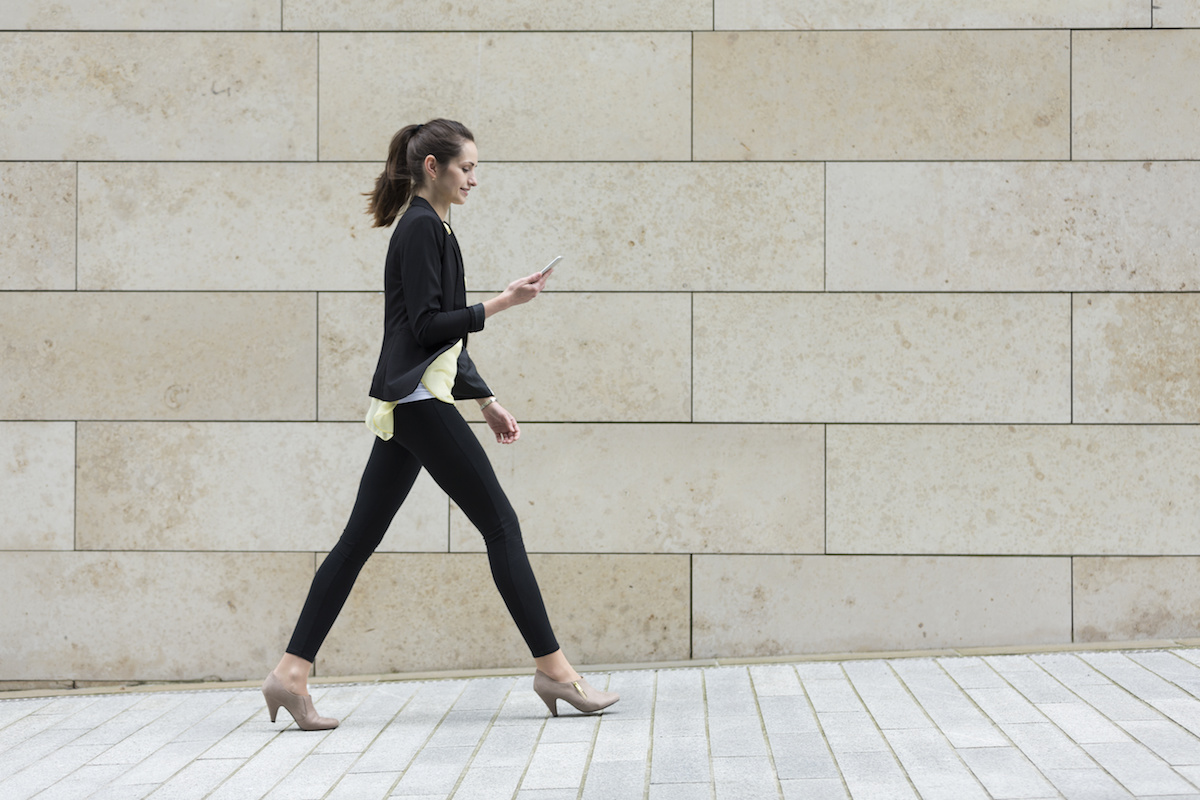 Woman looking at phone while walking on a brick path with a tile background