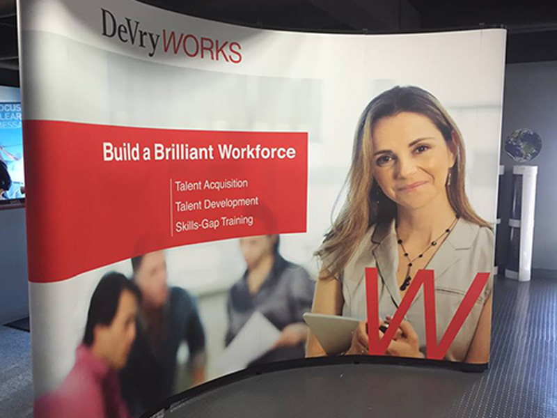 Tradeshow display featuring a banner for DeVry with image of woman with a clipboard 
