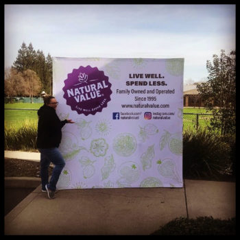person next to a Natural Value banner