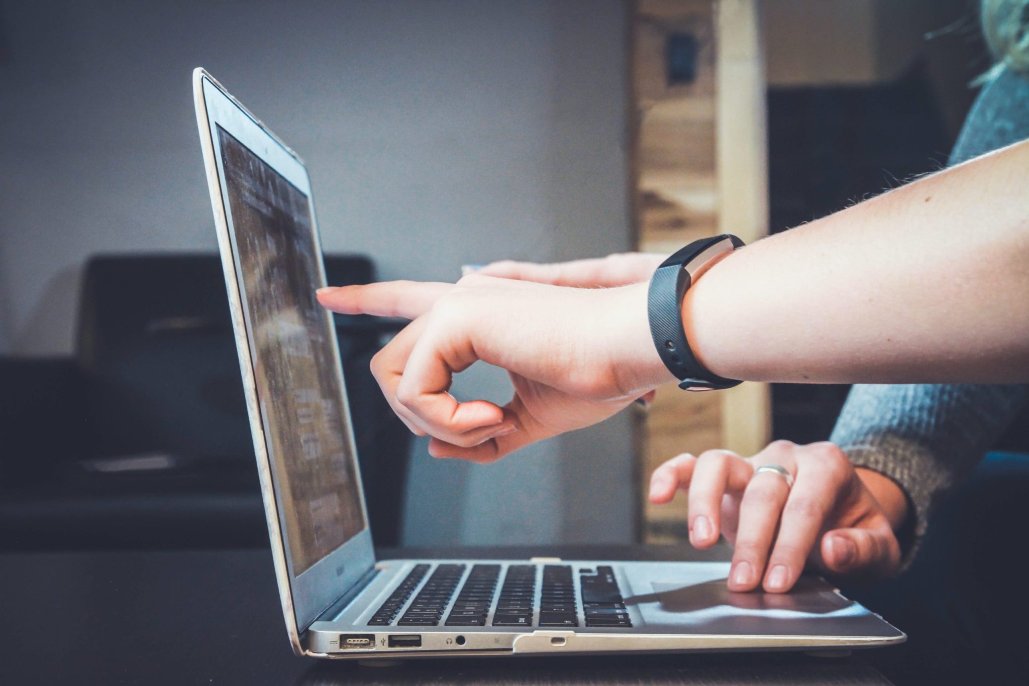 A finger points at a laptop screen demonstrating electronic device interaction.