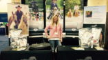 Trade show display for Optimum Performance equine nutrition featuring standing woman, vertical banners, and product bags.